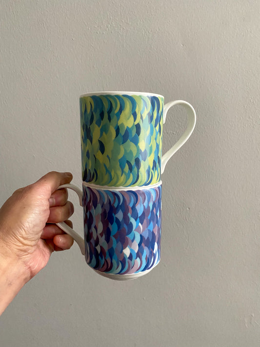 Two stacking mugs with mathematical circle pattern, stacked on top of each other. The bottom mug has the purple/blue colour way. The top mug has the green/yellow colourway.